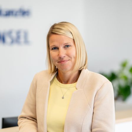 Die Junge Frau steht am Empfang im Büro und lächelt freundlich.